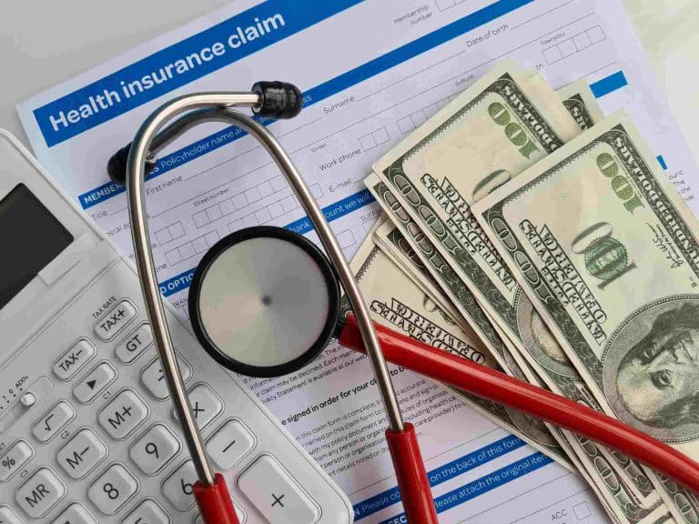Stethoscope, $100 bills, and calculator on top of insurance claim form